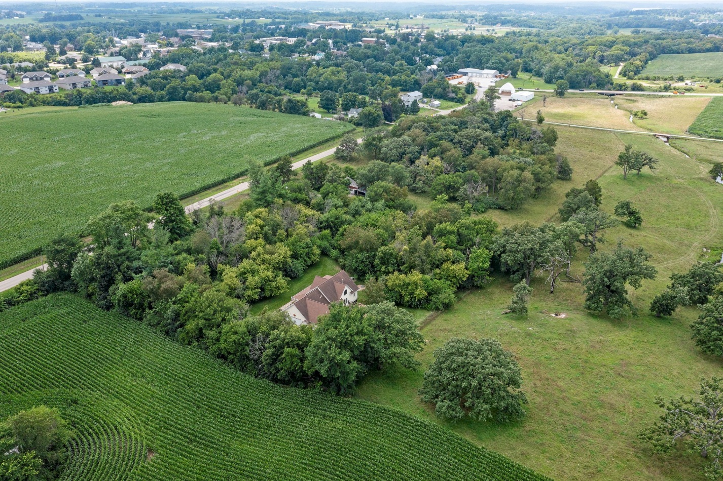 Aerial view of the wooded home and surrounding open land